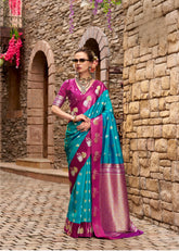 Woman in a colorful saree standing against a stone wall.
