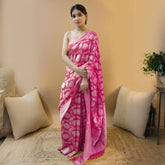 Woman in a dark pink jacquard work saree with golden motifs standing indoors in a room with beige curtains and traditional woven decor elements