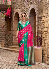 Woman in a pink and green saree standing in front of a stone building with arches.