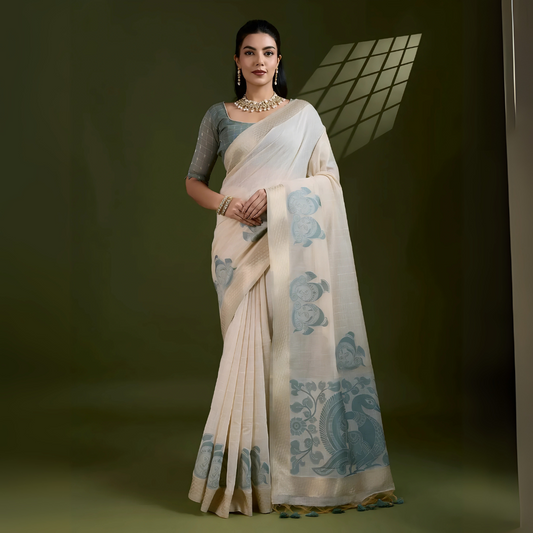 Woman wearing an ivory silk saree with grey fish and floral motifs, paired with a grey blouse and pearl jewelry, posing in a contemporary studio with olive green walls and a metal chair.