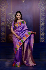 Woman wearing a purple saree with colorful patterns against a decorative purple background