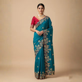 Woman wearing a blue saree with intricate patterns on a beige background
