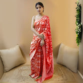 Woman in a red jacquard work saree with gold border standing indoors in a refined room with arched decor and vintage furniture accents