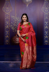 Woman in a red saree with green and yellow patterns against a decorative blue background