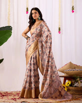 Woman wearing a patterned saree with a gold border against a white curtain background