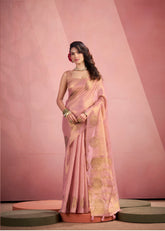 Woman wearing a pink and white saree against a stone wall.
