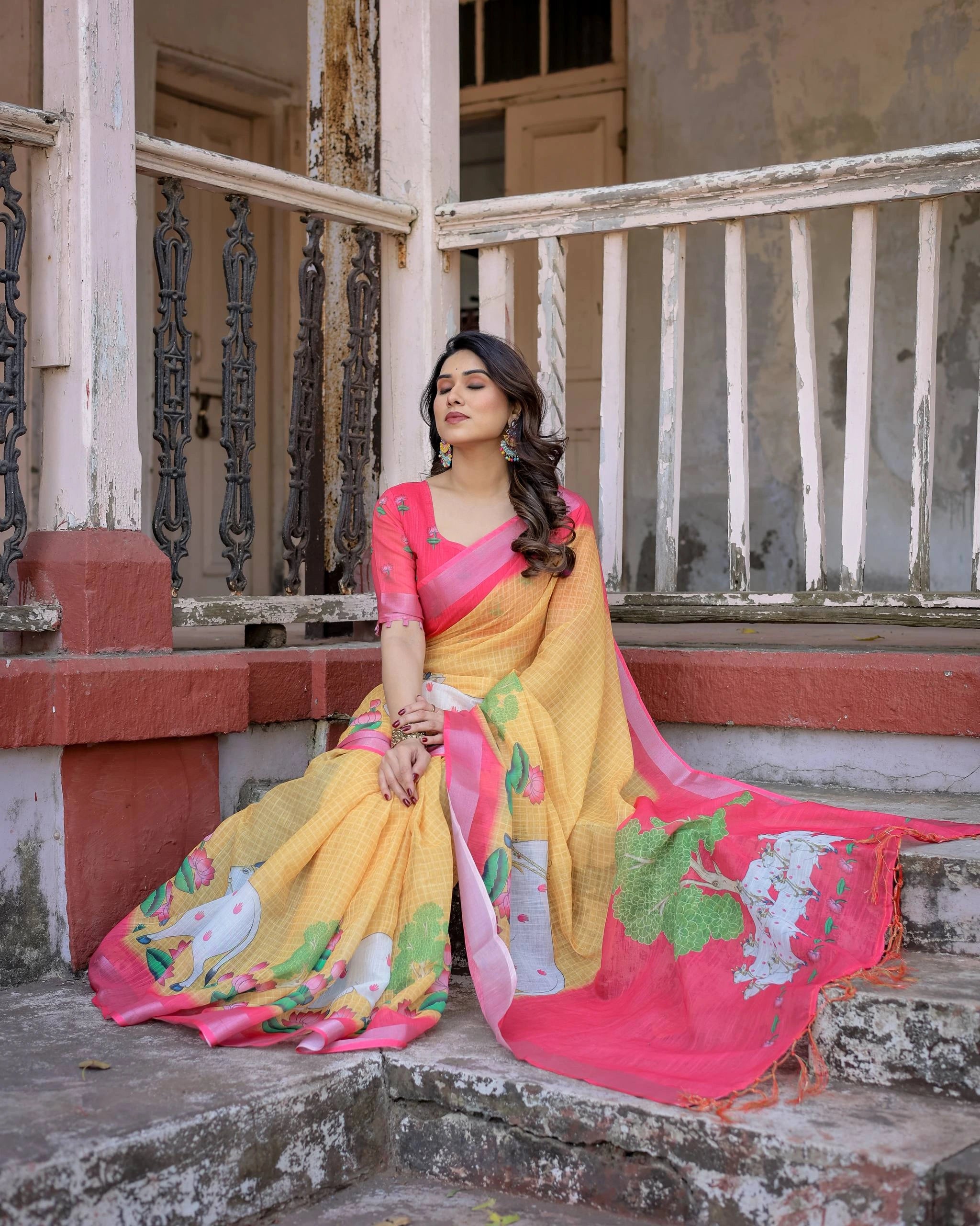 Woman in a yellow and pink saree sitting on steps with a dilapidated building in the background
