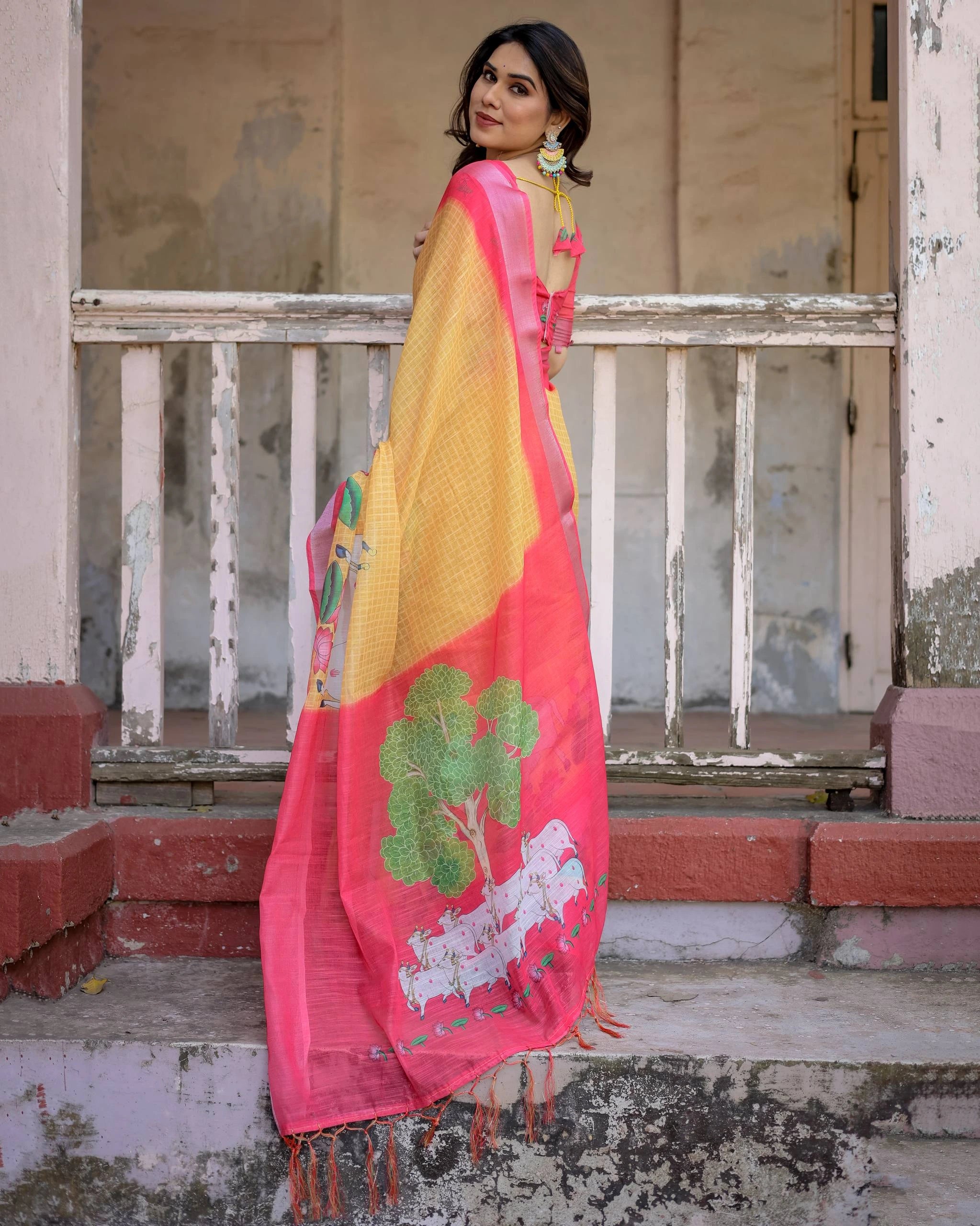 Woman wearing a colorful traditional outfit with a yellow and pink shawl in front of a dilapidated building.