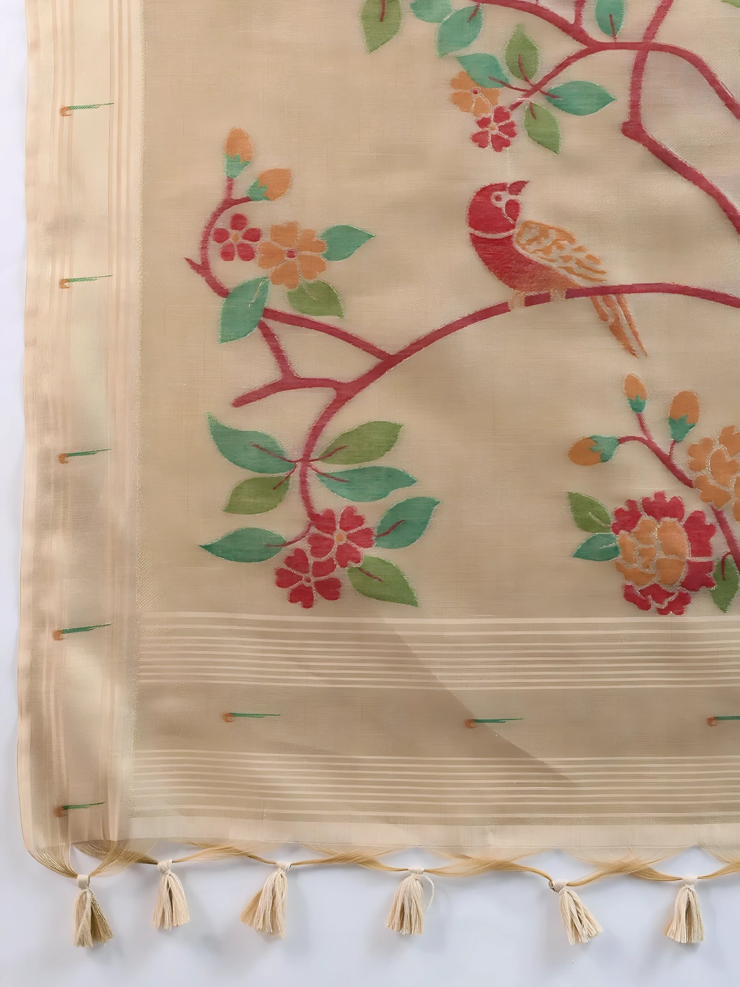Woman wearing an elegant beige silk saree featuring delicate floral motifs and a hand-painted pallu, paired with a sleeveless red blouse and traditional jewelry, gracefully posing in a modern studio with olive green walls and patterned window light.