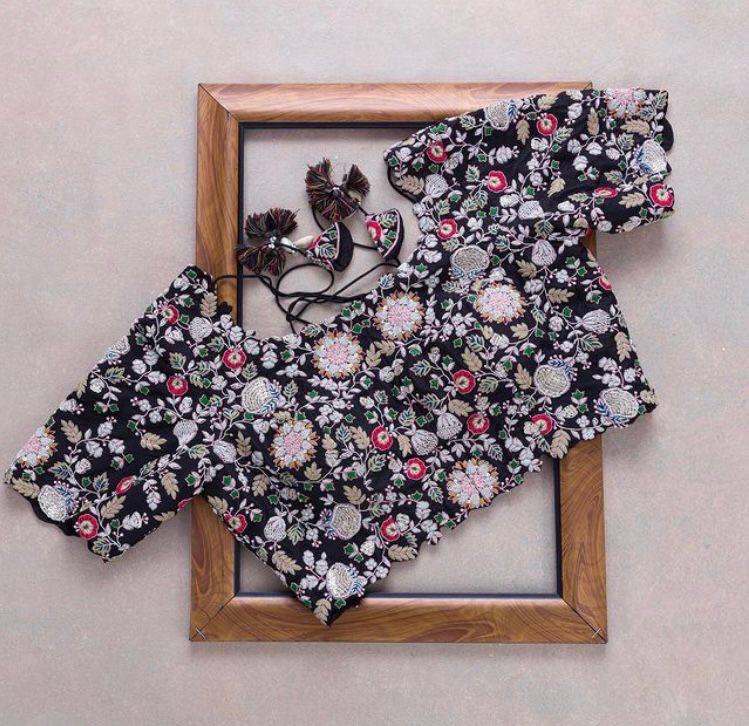 Black blouse with intricate embroidery work displayed within a wooden frame, featuring colorful floral patterns