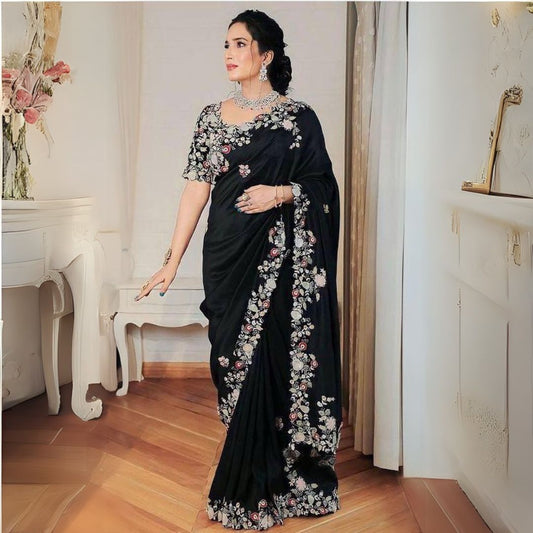 Woman wearing a black embroidery work saree with intricate patterns, standing in a lush outdoor setting