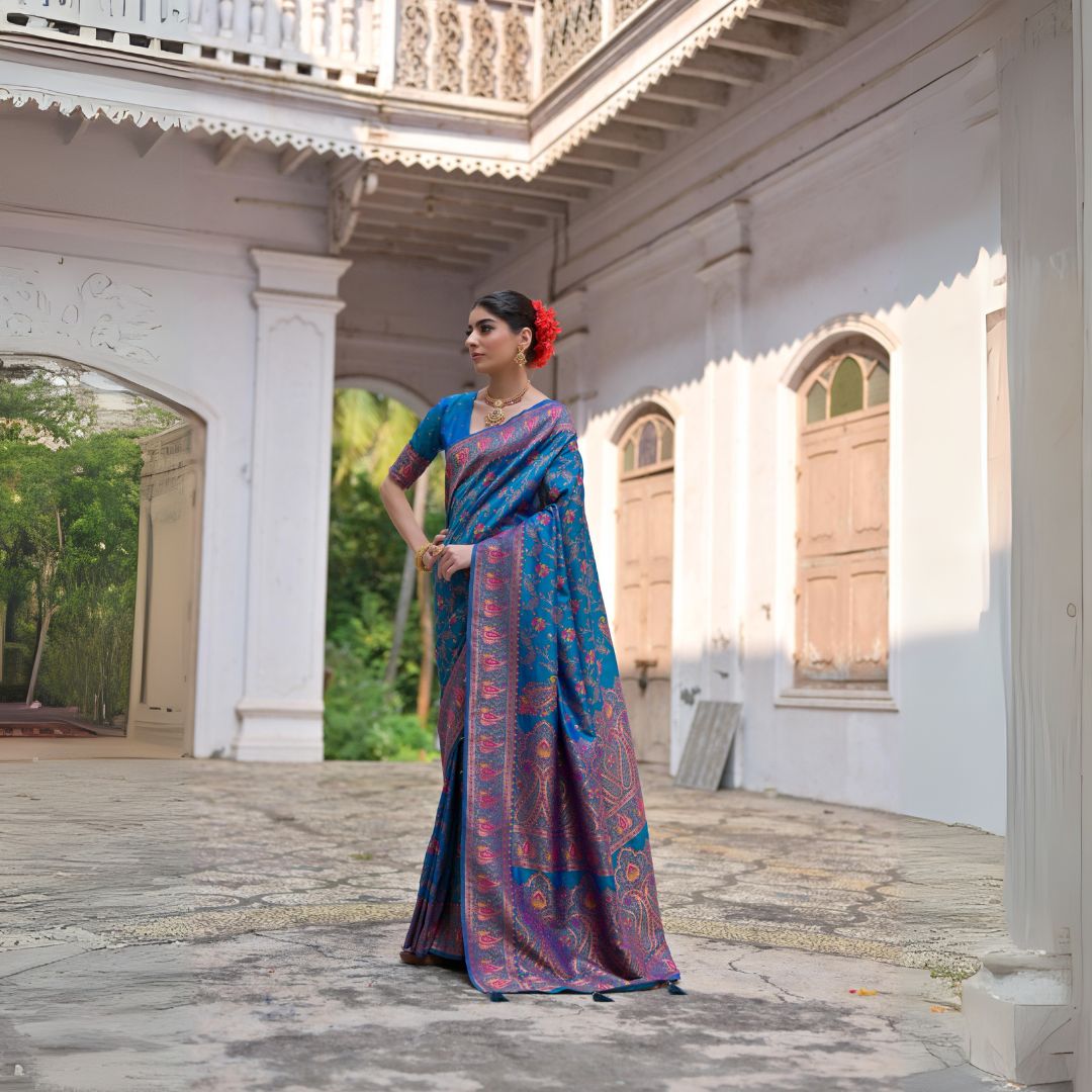 Woman wearing a blue zari work saree with intricate designs in a traditional courtyard