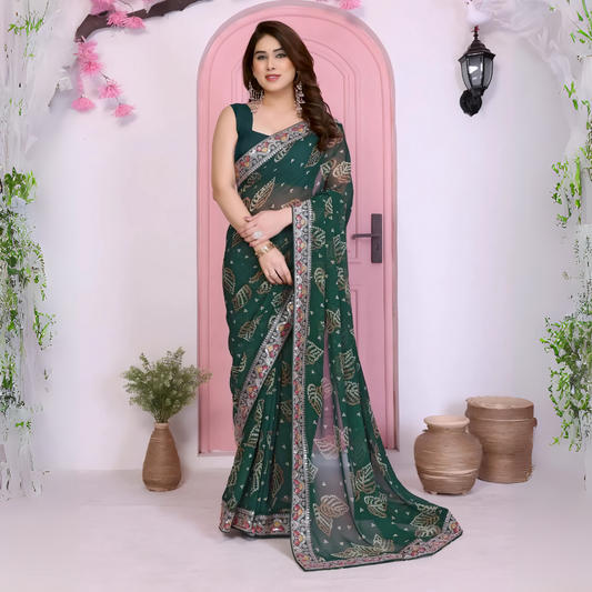 Woman wearing a dark green printed saree with traditional leaf motifs and an ornate multicolor embroidered border, paired with a matching blouse. She stands gracefully in front of a pastel pink arched doorway, accessorized with statement earrings and bangles, with earthy clay pots, a green foliage vase, and decorative pink branches adding a contemporary touch to the minimalist studio setting.