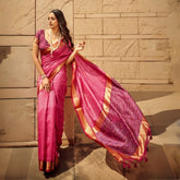 Woman wearing elegant dark pink saree with intricate zari work and patterned pallu standing against stone wall