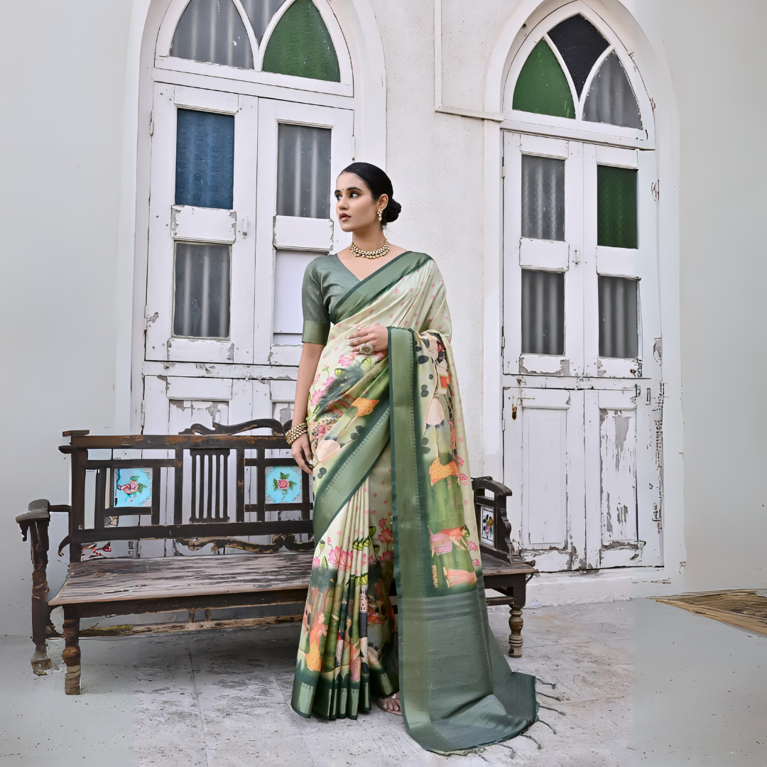 Woman wearing a green floral saree with intricate patterns and a matching green blouse, accessorized with traditional gold jewelry including a statement necklace, standing beside a vintage wooden bench in front of weathered white doors with green and blue stained glass panels in a heritage-style courtyard setting.