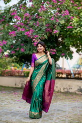 Woman wearing elegant green zari work saree with rich purple blouse and gold jewelry in a floral garden setting
