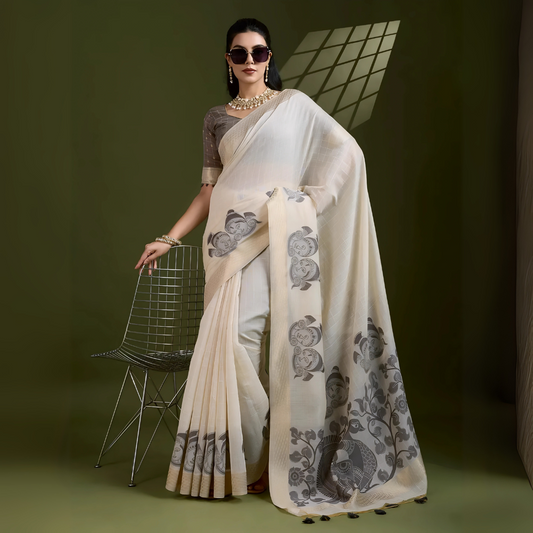 Woman wearing an ivory silk saree with grey fish and floral motifs, paired with a grey blouse and pearl jewelry, posing in a contemporary studio with olive green walls and a metal chair.