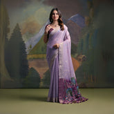 Woman wearing a lavender silk saree with intricate peacock embroidery and floral motifs on the pallu, paired with a matching blouse and traditional jewelry, standing in front of a painted mountain and forest backdrop.