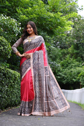 Woman wearing traditional red Madhubani print saree with intricate designs and ethnic jewelry in a green outdoor setting