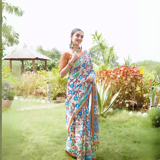 Woman wearing a multicolor Madhubani-printed saree with vibrant floral and abstract motifs, paired with a brown blouse and traditional jewelry, standing gracefully on a lush green lawn surrounded by tropical plants and red foliage, with a garden gazebo in the background.