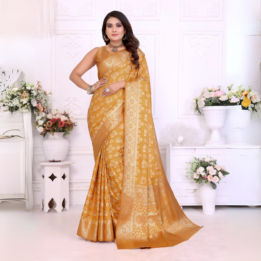 Woman wearing a mustard yellow Banarasi silk saree featuring intricate gold traditional motifs and a shimmering woven border, paired with a matching blouse and statement jewelry. She poses elegantly in a classic white room adorned with ornate wall panels and decorative vases overflowing with pastel and white artificial flowers.