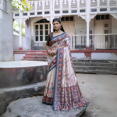 Woman wearing an off-white silk saree with blue and red Patola-inspired geometric and floral borders, featuring intricate floral motifs, paired with a matching blouse and traditional jewelry, elegantly posing on stone steps in front of a vintage heritage house with ornate wooden railings and classic architecture.Woman wearing an off-white silk saree with blue and red Patola-inspired geometric and floral borders, featuring intricate floral motifs, paired with a matching blouse and traditional jewelry, elegan