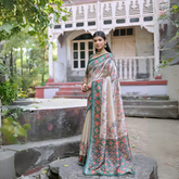 Woman wearing an off-white silk saree with green Patola-inspired geometric and floral borders, featuring intricate floral motifs, paired with traditional jewelry, elegantly posing on stone steps in front of a vintage heritage house with ornate wooden railings and lush greenery in the background.