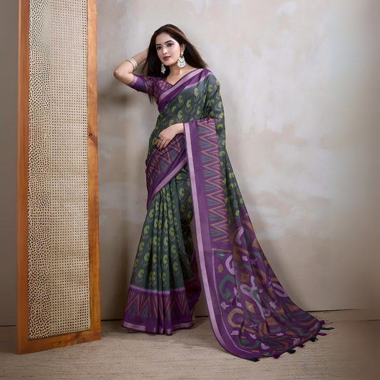 Woman wearing an olive green saree adorned with purple geometric patterns and bold abstract motifs, paired with a matching blouse and statement silver earrings. She poses elegantly in a contemporary studio setting against a neutral textured wall, with a tall woven screen and rustic wooden flooring, showcasing the saree’s vibrant pallu and intricate design.