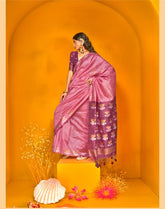 Woman dressed in pink zari work saree with floral motifs and tassel border, styled with traditional jewellery, posing in a vibrant yellow arched backdrop