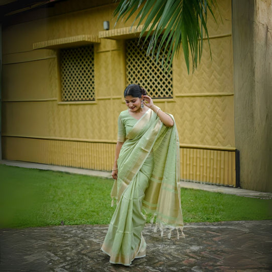 Woman in pista-colored zari work saree standing outdoors near a yellow building and palm leaves