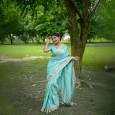 Woman in a powder blue saree with zari work posing in a park near a tree