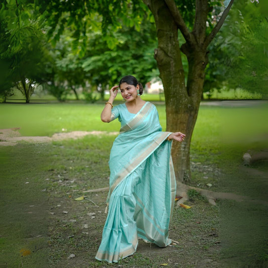 Woman in a powder blue saree with zari work posing in a park near a tree