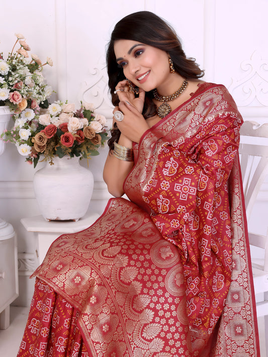 Woman draped in a vibrant red Banarasi bandhani saree featuring intricate white tie-dye patterns and an ornate zari border, paired with a matching short-sleeve blouse and traditional jewelry. She stands gracefully in a classic white room adorned with paneled walls and elegant white vases filled with pastel and rose-toned artificial flower arrangements.