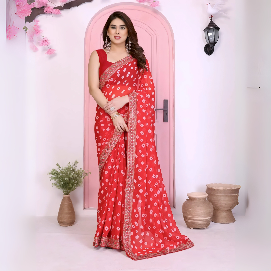 Woman wearing a vibrant red bandhani saree adorned with traditional white tie-dye patterns and a gold embroidered border, paired with a matching sleeveless blouse and accessorized with statement earrings and bangles. She stands gracefully in front of a pastel pink arched doorway, surrounded by earthy clay pots, a green foliage vase, and decorative pink branches in a modern studio setting.