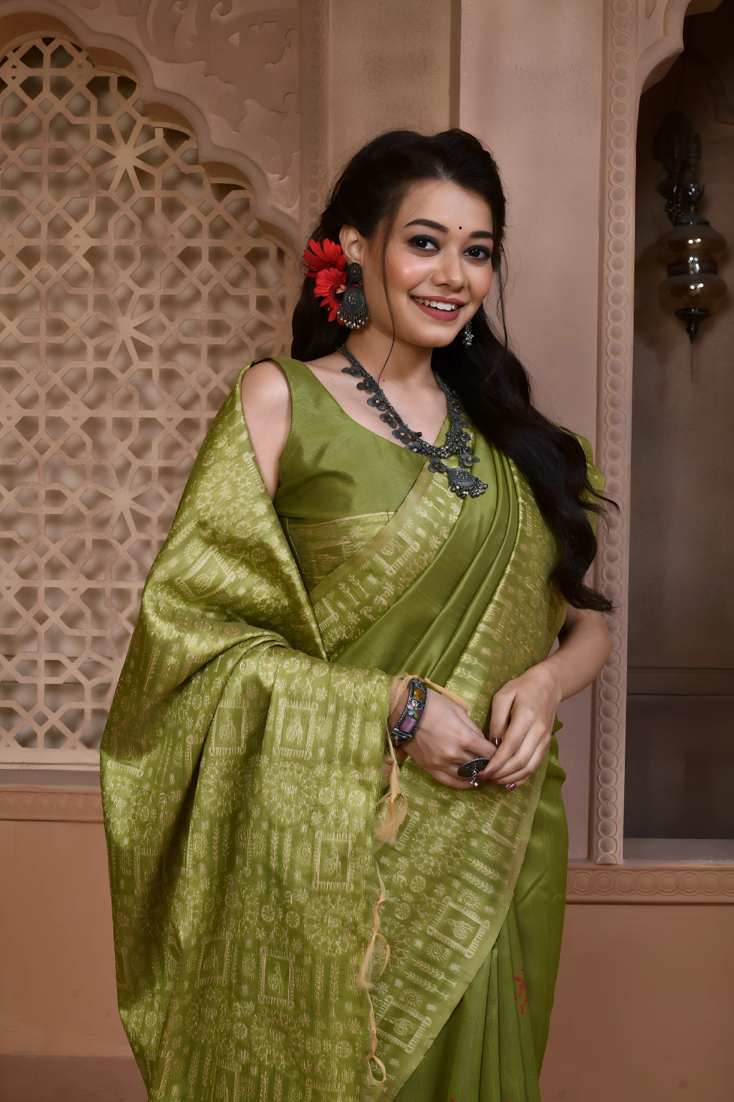 Woman wearing a light green silk saree with an intricate geometric border and pallu, paired with traditional jewelry, standing in a heritage-inspired room with ornate carved window and pastel walls