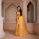 A woman models a vibrant Yellow Banglori Raw Silk Saree. The pallu and border feature dense, tone-on-tone Kalamkari-style weaving in gold Zari. She wears a yellow blouse and heavy dark gemstone jewelry, posing in an ornate, traditional setting.