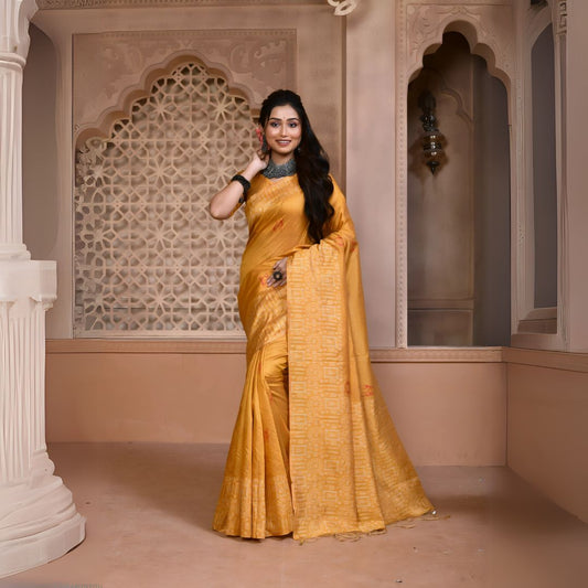 A woman models a vibrant Yellow Banglori Raw Silk Saree. The pallu and border feature dense, tone-on-tone Kalamkari-style weaving in gold Zari. She wears a yellow blouse and heavy dark gemstone jewelry, posing in an ornate, traditional setting.