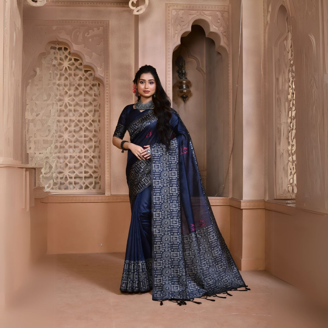 Woman wearing a navy blue silk saree with geometric patterned border and pallu, paired with traditional jewelry, standing in a heritage-inspired room with ornate carved windows and pastel walls