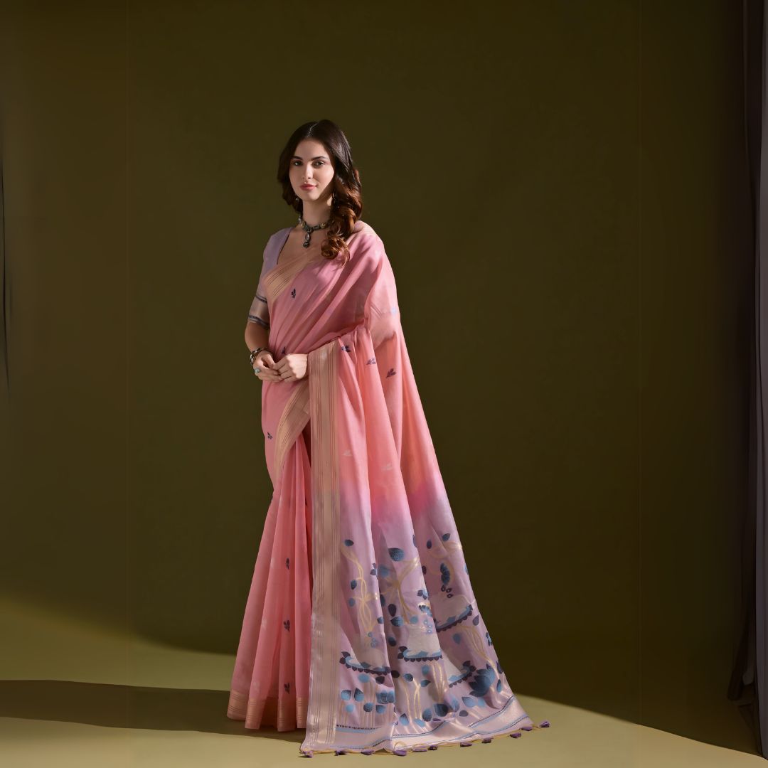 Woman wearing a pink silk saree with floral print and a statement necklace, standing against an olive green background.