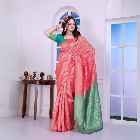 A woman models a striking Pink Banarasi Silk Saree with dense all-over gold Zari weaving. The pallu provides a dramatic contrast in sea green with heavy gold weaving. She wears a sea green blouse and gold jewelry, and has flowers in her hair.