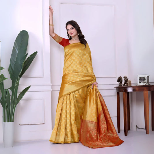 A woman models a striking Golden Yellow Banarasi Silk Saree with dense tone-on-tone Zari weaving. The wide border and pallu feature a dramatic contrast in vibrant red/orange with heavy gold Banarasi weaving. She wears a red blouse and gold Kundan jewelry.