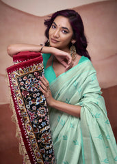 Woman in a light green saree holding a decorative fabric against a plain background