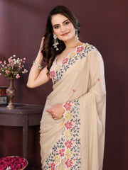 Woman wearing a beige saree with floral embroidery against a dark background