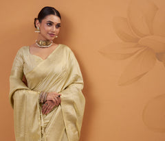 Woman in a light yellow saree against a brown background