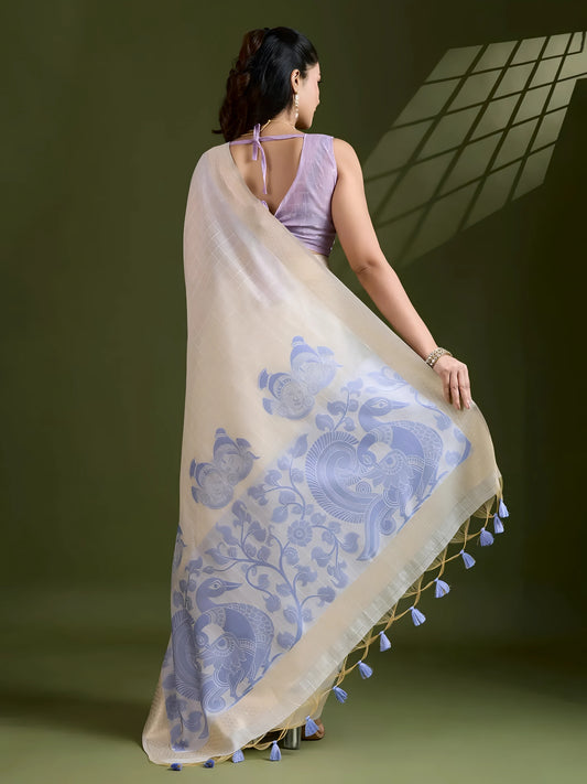 Woman wearing an ivory silk saree with blue floral motifs and a lavender blouse, accessorized with pearl jewelry, posing in a contemporary olive green studio with a geometric window shadow on the wall.