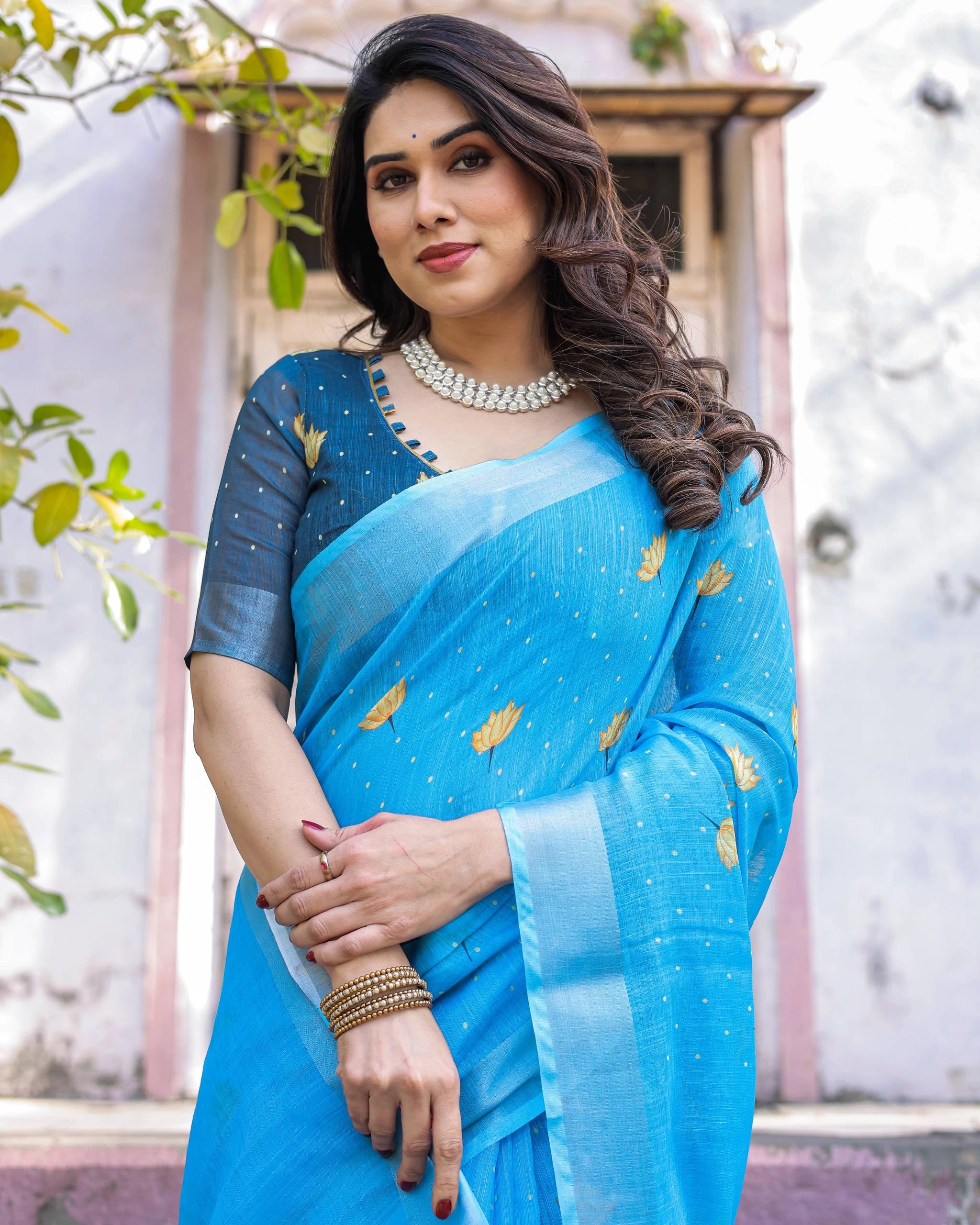 Woman wearing a blue saree with a floral pattern, standing outdoors.