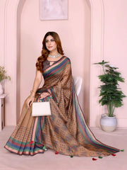 Woman wearing a beige silk saree adorned with subtle multicolor stripes and small dot patterns, paired with a sleeveless dark blouse and traditional jewelry including a statement necklace, bangles, and rings. She stands gracefully in a contemporary studio setting featuring a pastel arched alcove, a white side table with a floral vase, and a large potted green plant, showcasing elegant and understated ethnic style.