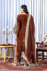 Woman in a brown traditional outfit with a matching dupatta standing in a decorated room.