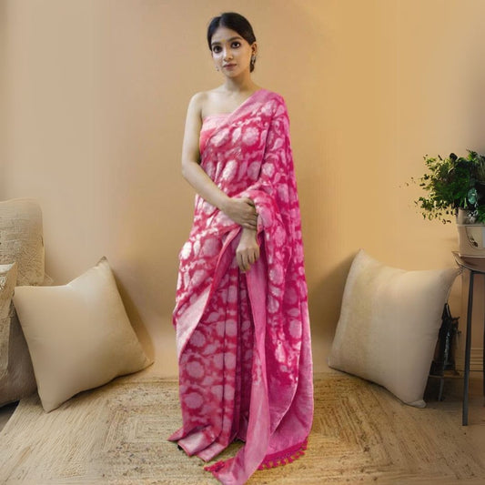 Woman in a dark pink jacquard work saree with golden motifs standing indoors in a room with beige curtains and traditional woven decor elements