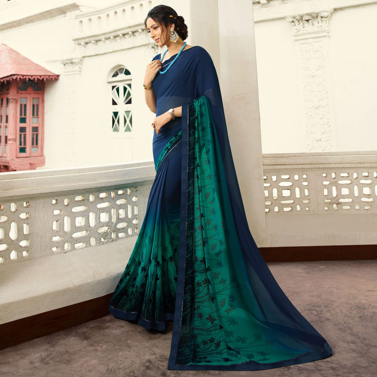 Woman in a dark turquoise jacquard work saree with gold border standing indoors in an elegant room with arched decor and vintage furniture elements